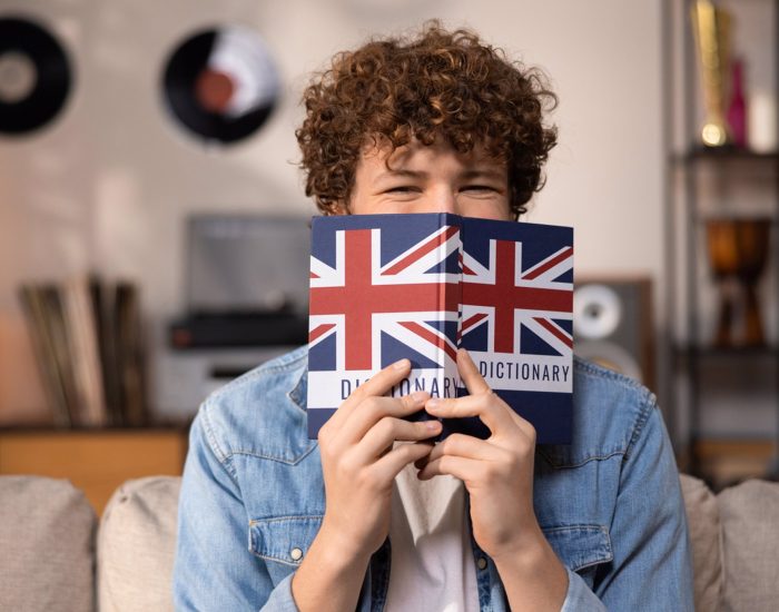 A teenager with curly hair sits focused in a room studying for an English exam. A boy in a blue jean shirt prepares for an English job interview.