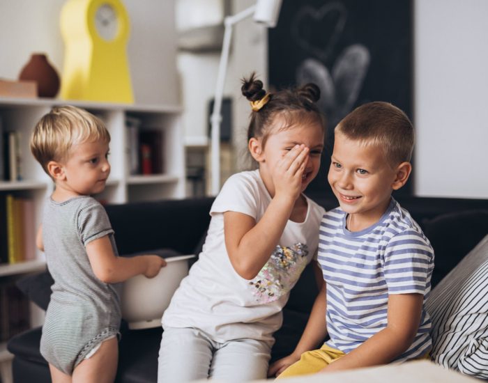 sister whispering to her brother, other brother looking, at home