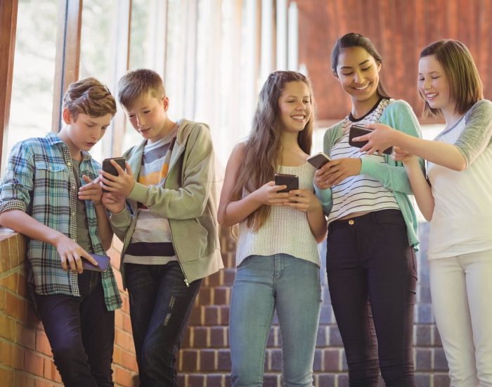 Group of smiling school friends using mobile phone in corridor at school