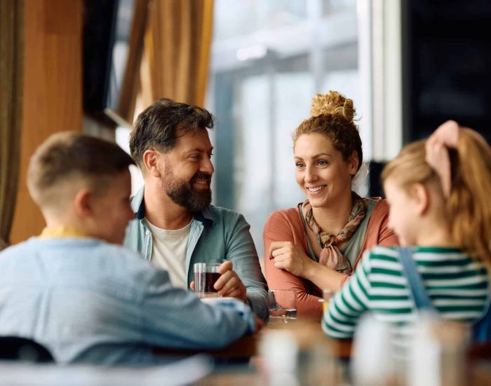 Happy parents communicating with their children while having a meal in a restaurant.