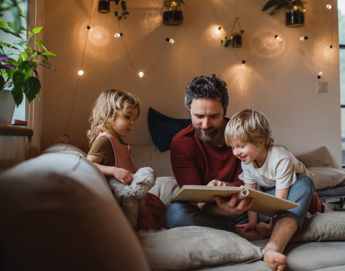 A mature father with two small children resting indoors at home, looking at photo album.